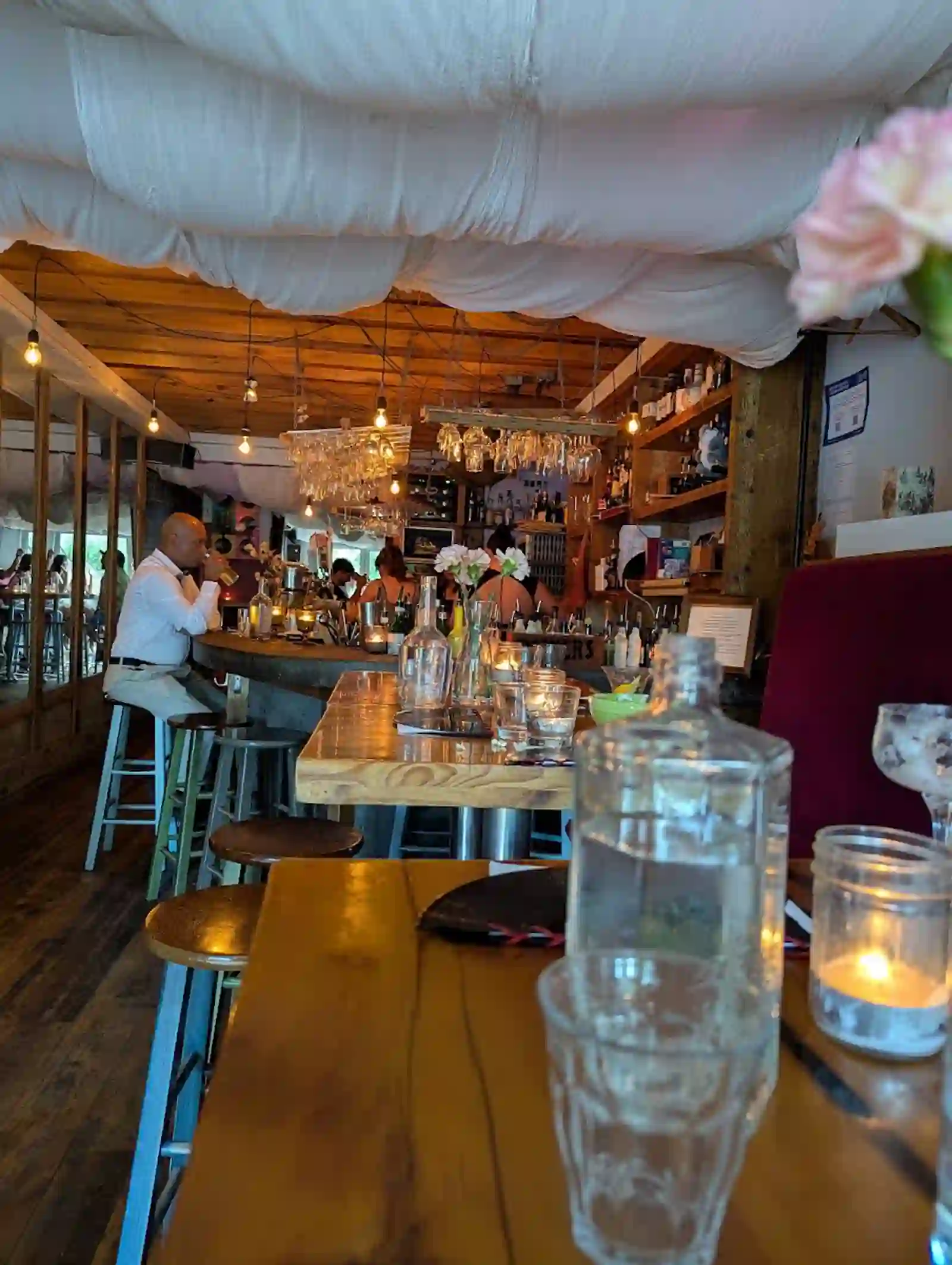 Dim lounge interior with draped fabric ceiling, warm Edison bulbs, candlelight and bar seating